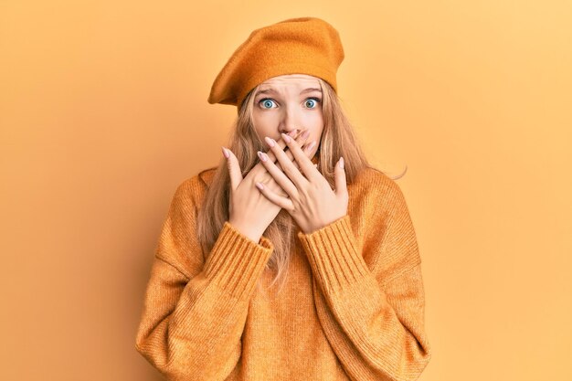 Beautiful young caucasian girl wearing french look with beret shocked covering mouth with hands for mistake. secret concept.