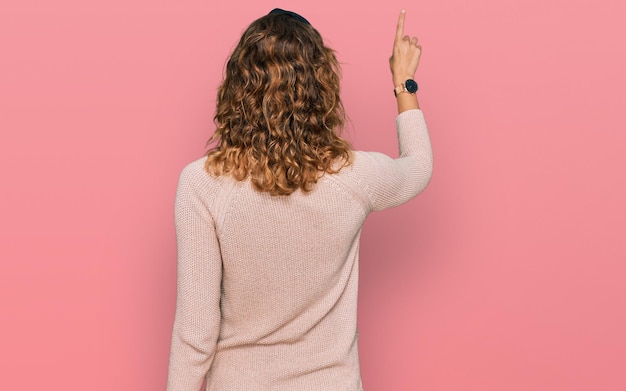 Foto gratuita bella giovane donna caucasica che indossa un maglione casual che posa all'indietro puntando in avanti con la mano del dito