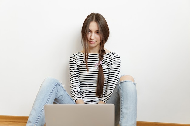 Beautiful young Caucasian woman with messy hairstyle using generic laptop