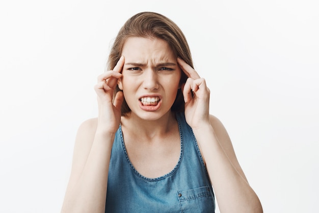 Beautiful young charming dark-haired european woman squeezing forehead with fingers,  with unhappy expression, suffering from terrible headache