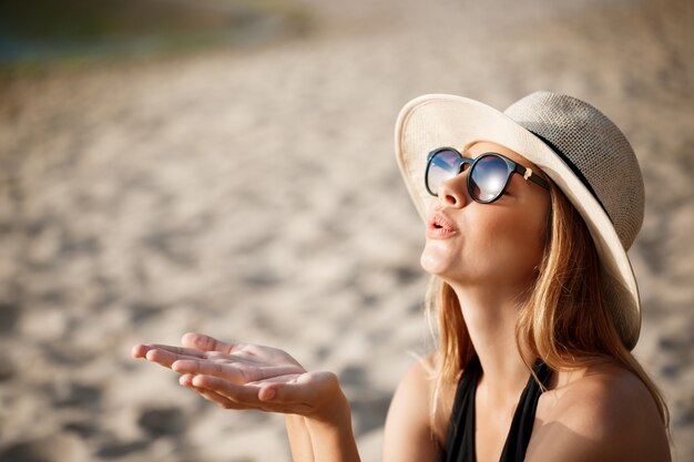 안경과 모자를 쓰고 아름다운 젊은 명랑 소녀는 아침 해변에서 휴식