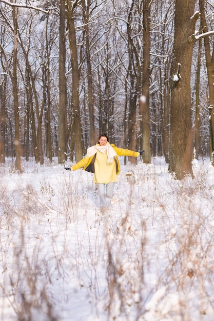 雪景色の冬の森の美しい若い陽気な女性は、冬に喜び、暖かい服を着て雪を楽しんでいます