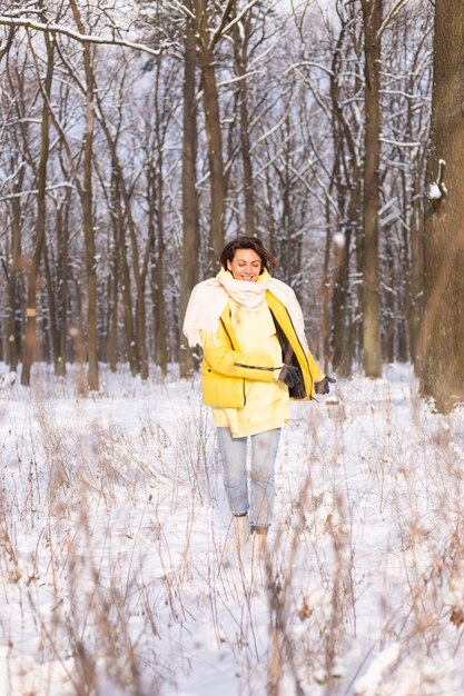 雪景色の冬の森の美しい若い陽気な女性は、冬に喜び、暖かい服を着て雪を楽しんでいます