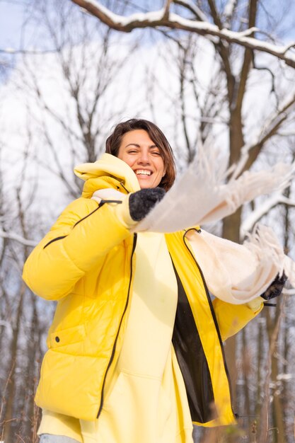 Beautiful young cheerful woman in a snowy landscape winter forest having fun rejoices in winter and snow in warm clothes
