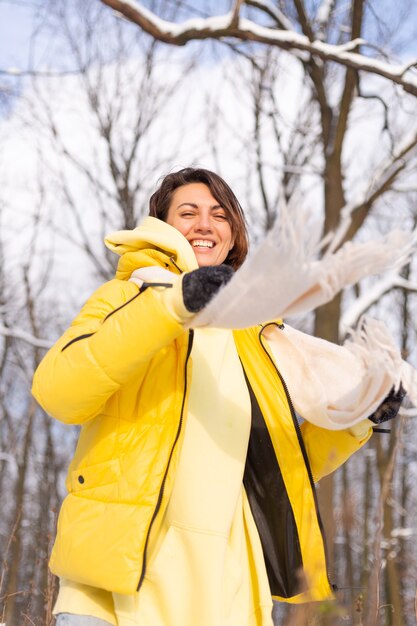 雪景色の冬の森の美しい若い陽気な女性は、冬に喜び、暖かい服を着て雪を楽しんでいます