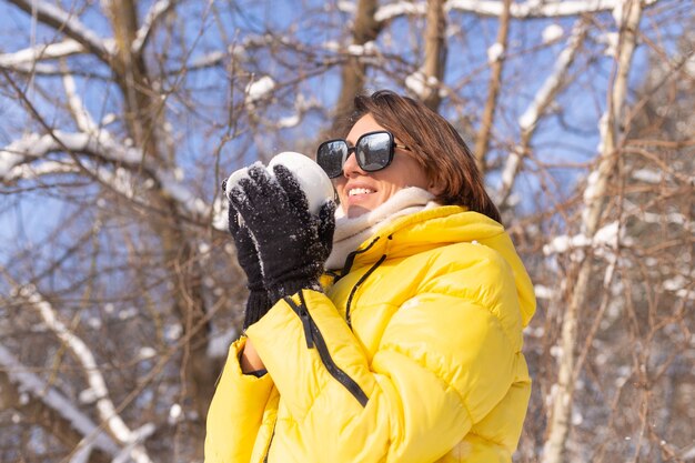 雪に覆われた風景の冬の森の美しい若い陽気な女性は、楽しんで雪で満たされたカップとサングラスで