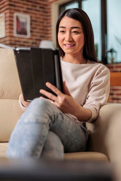 집에서 디지털 태블릿을 사용하는 아름다운 젊은 중국 여성, 소파 엔터테인먼트 장치에 앉아 웃고 있는 인터넷 웹 3.0 연결, 인터넷 무선 장치 컴퓨터 태블릿 탐색