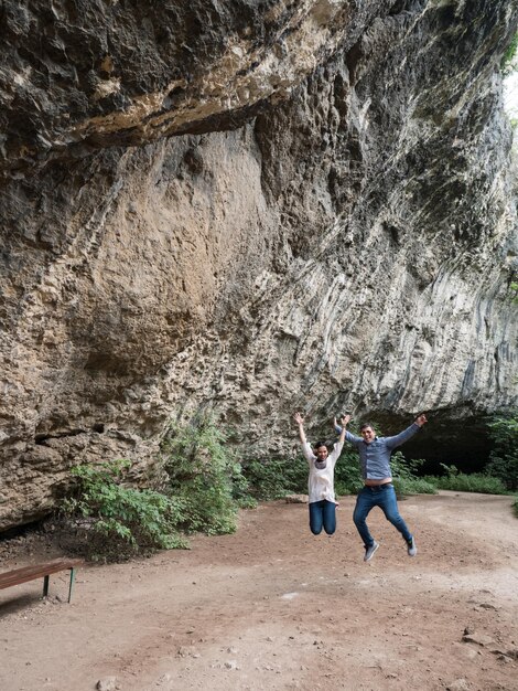 Beautiful young couple jumping in the air of happiness in front of a cave. Couple in nature.