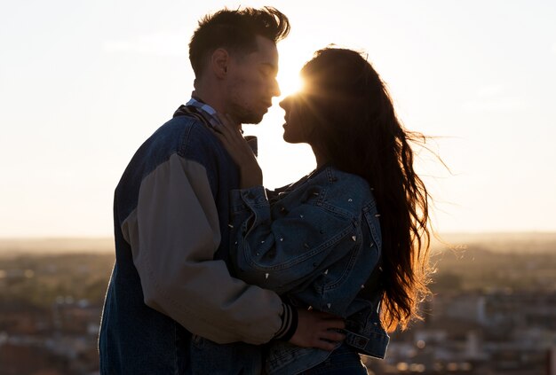 Beautiful young couple in love standing at a building rooftop at the sunset.