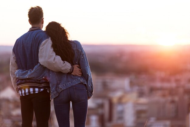 Beautiful young couple in love standing at a building rooftop at the sunset.