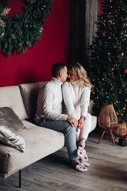 恋人たちの美しい若いカップルは、クリスマスの雰囲気の中で自宅のソファでキスします