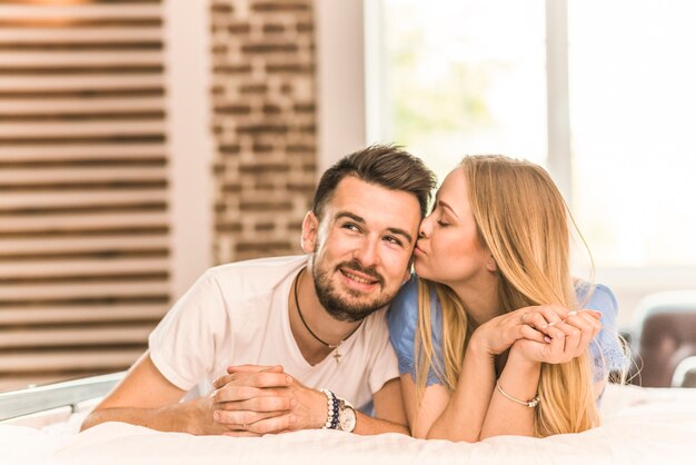 Beautiful young couple lying on bed kissing