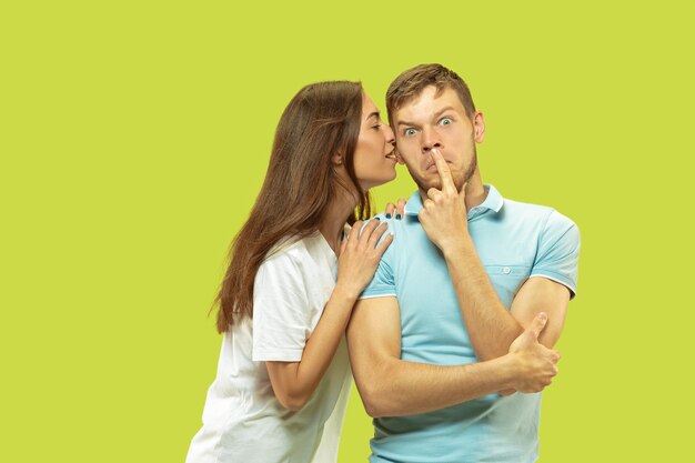 Beautiful young couple's half-length portrait isolated on green  space. Woman and man standing, caddling and kissing 