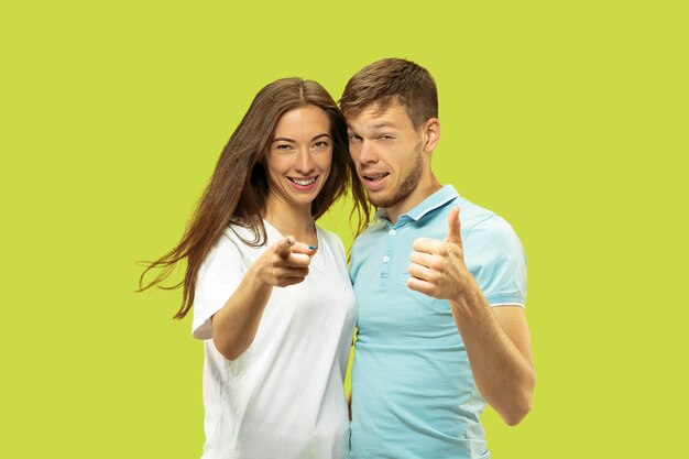 Beautiful young couple's half-length portrait isolated. Woman and man standing and pointing up, showing the sing of OK. Facial expression, human emotions concept.