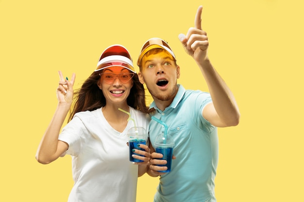 Beautiful young couple's half-length portrait isolated. Woman and man standing with drinks in colorful caps. Facial expression, summer, weekend concept. Trendy colors.