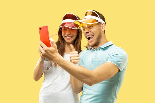 Beautiful young couple's half-length portrait isolated. Woman and man standing with drinks making selfie. Facial expression, summer, weekend concept. Trendy colors.