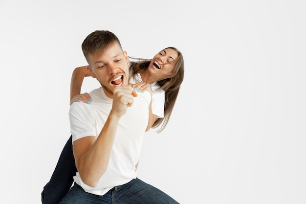 Beautiful young couple's portrait isolated on white studio background. Facial expression, human emotions, advertising concept. Copyspace. Woman and man dancing and singing, look happy together.