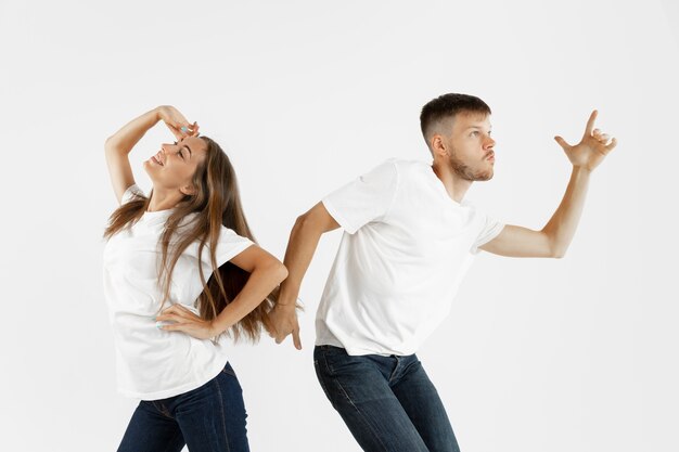Beautiful young couple's portrait isolated on white studio background. Facial expression, human emotions, advertising concept. Copyspace. Woman and man dancing and smiling, pointing, look cool.