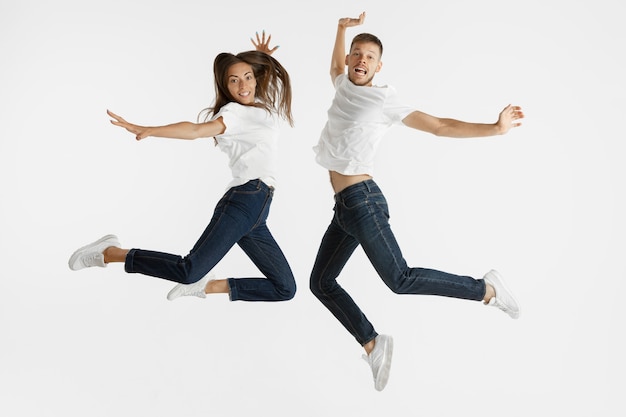 Beautiful young couple's portrait isolated on white studio background. Facial expression, human emotions, advertising concept. Copyspace. Woman and man jumping, dancing or running together.