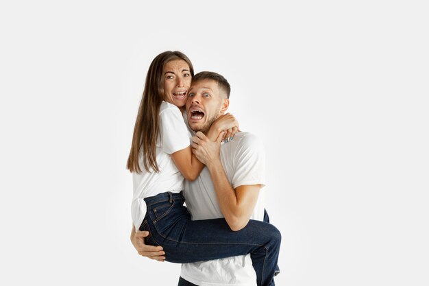 Beautiful young couple's portrait isolated on white studio background. Facial expression, human emotions, advertising, relation concept. Man and woman holding each other, look scared, screaming.