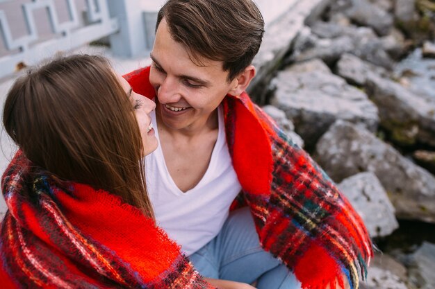 Beautiful young couple sitting on a stone embankment, wrapped in a blanket