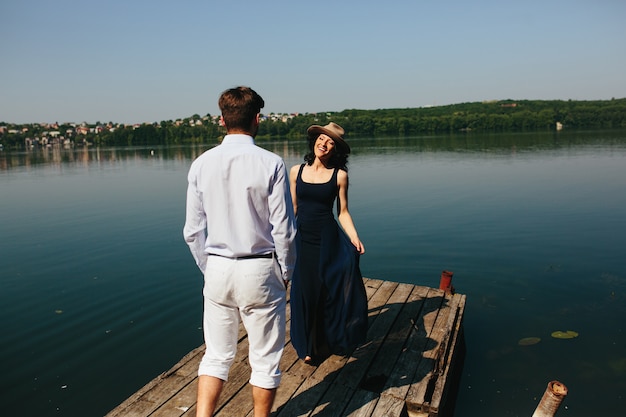 Free photo beautiful young couple spends time on the wooden pier on the lake