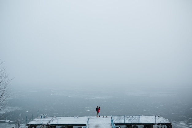 Free photo beautiful young couple standing on a pier and looks at the frozen lake