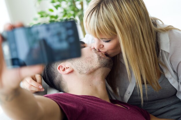 Beautiful young couple using mobile phone at home.