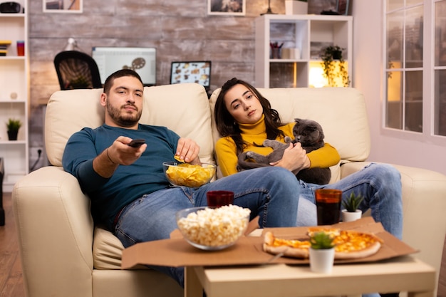 Бесплатное фото Красивая молодая пара смотрит телевизор и ест фаст-фуд на вынос в гостиной