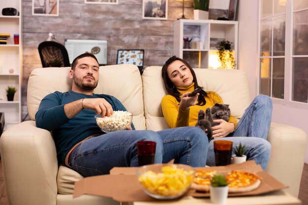 テレビを見たり、リビングルームでファーストフードのテイクアウトを食べている美しい若いカップル