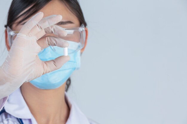 Beautiful young doctor is wearing mask while holding medicine with rubber gloves on gray wall.
