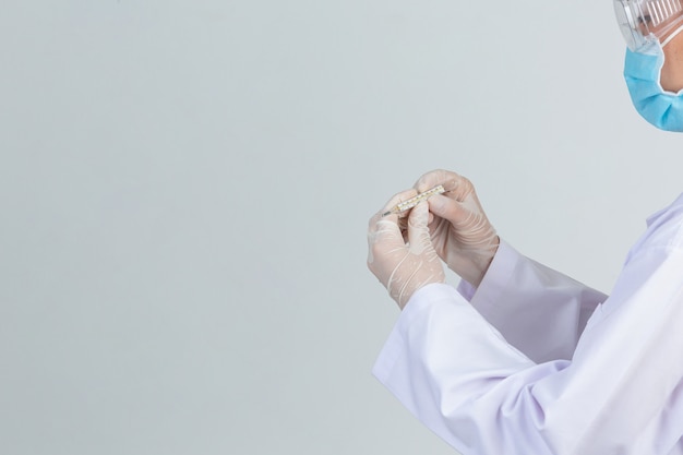 Free photo beautiful young doctor is wearing mask while holding thermometer with rubber gloves on gray wall.