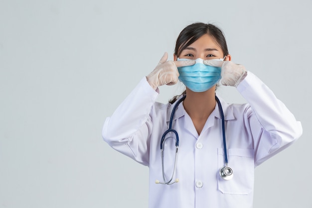 美しい若い医者は白い壁に人差し指を上げている間マスクを着ています。