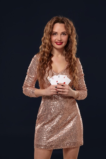 Bella giovane donna emotiva in abito da cocktail che mostra le sue carte all'avversario, quattro di assi, mano migliore. sfondo nero, girato in studio