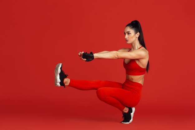 Beautiful young female athlete practicing on red studio wall