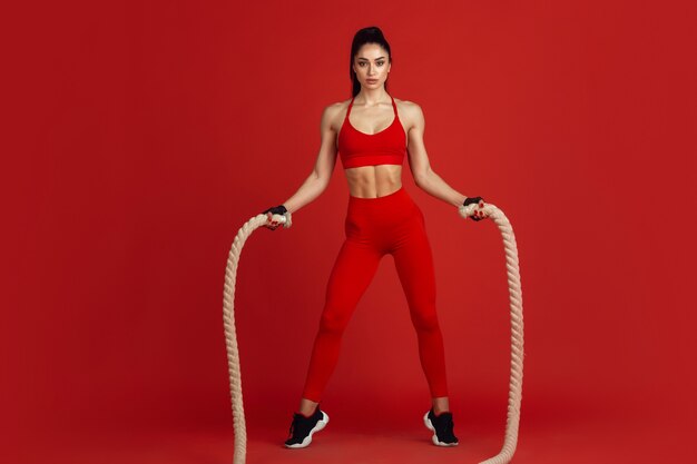 Beautiful young female athlete practicing on red studio wall