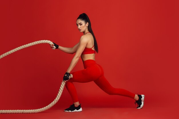 Beautiful young female athlete practicing on red wall monochrome portrait