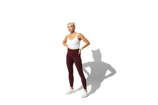 Beautiful young female athlete practicing on white studio wall, portrait with shadow.