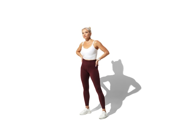 Beautiful young female athlete practicing on white studio wall, portrait with shadow.