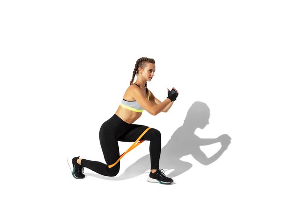 Beautiful young female athlete practicing on white studio wall with shadows