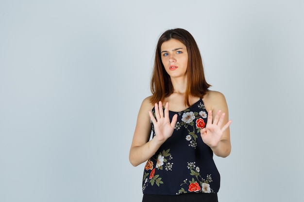 Beautiful young female in blouse showing stop gesture and looking scared