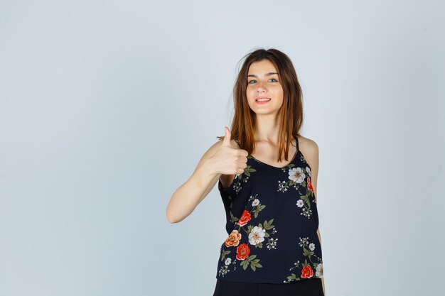Beautiful young female in blouse showing thumb up and looking cheerful