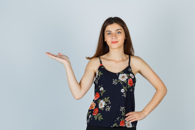 Beautiful young female in blouse showing welcoming gesture and looking confident