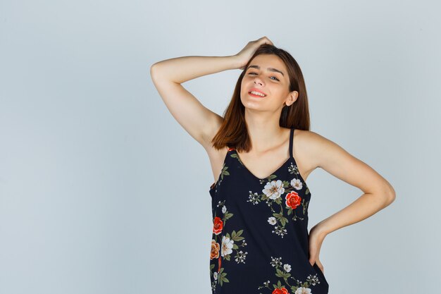 Beautiful young female holding hand on head in blouse and looking glad