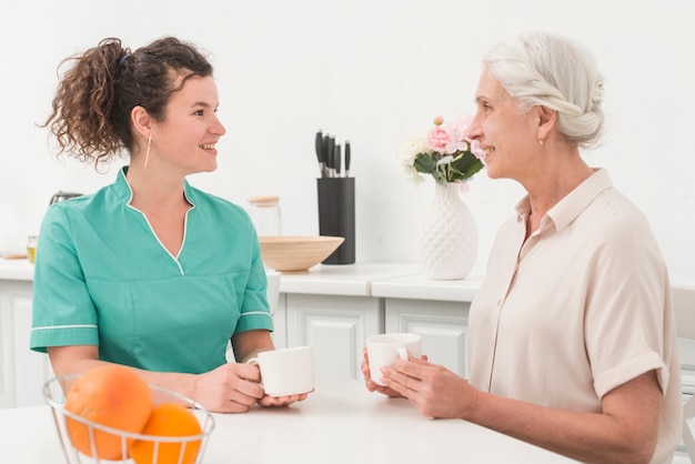 Beautiful young female nurse having coffee with senior woman