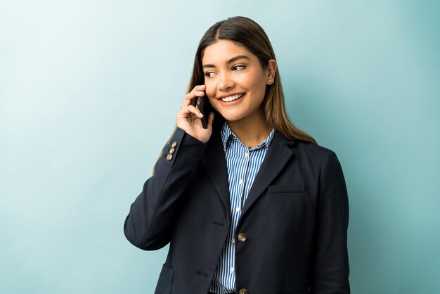 Beautiful young female professional talking on mobile phone while looking away and standing against colored background