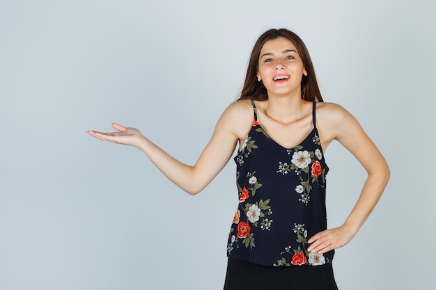 Beautiful young female showing welcoming gesture in blouse and looking happy