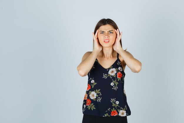 Beautiful young female suffering from strong headache in blouse and looking annoyed