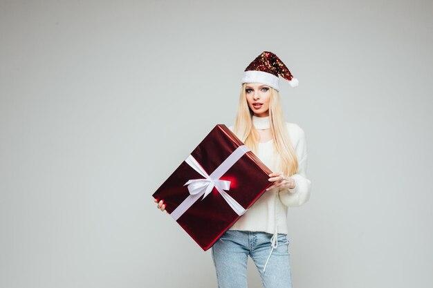 Beautiful young female with red and white christmas hat holds a big box with present and rejoices