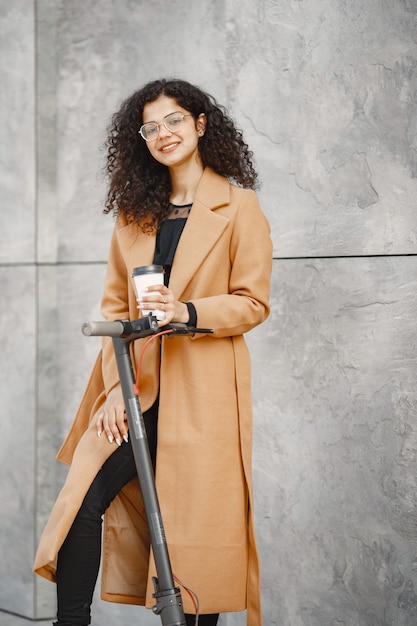 Free photo beautiful young girl in a brown coat. woman riding an electric scooter.